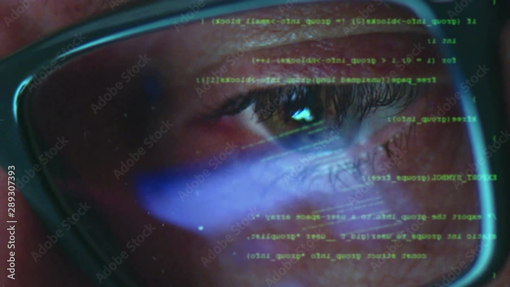 Male hacker working on a computer for cyber attack while green binary hacking code characters reflect on his face in a dark office room