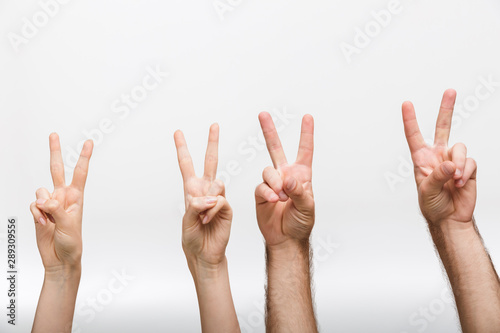Man's and woman's raised hands isolated over white wall background showing peace gesture.