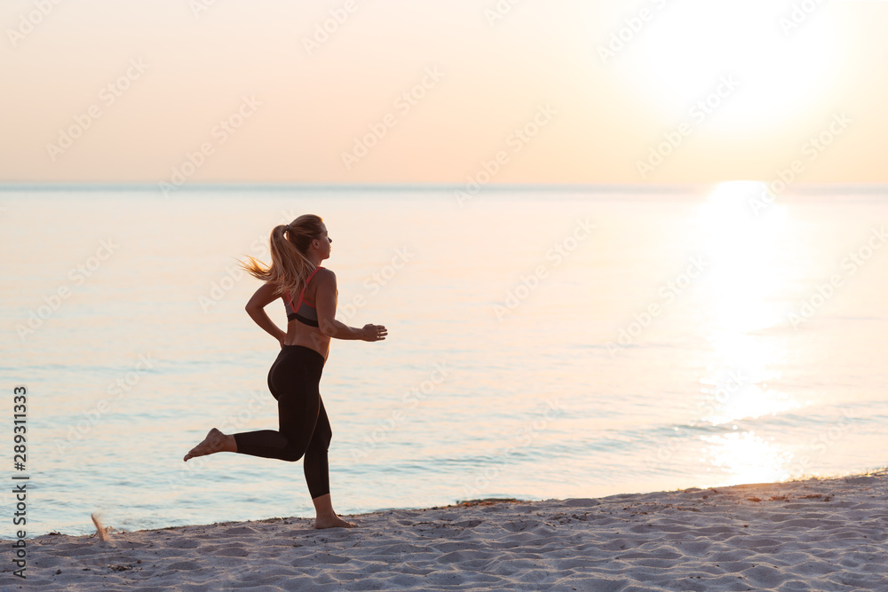 Fototapeta premium Young woman running on the beach at sunset