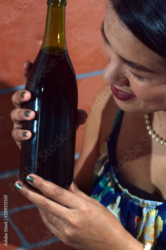 beautiful middle aged woman holding wine bottle close to her face