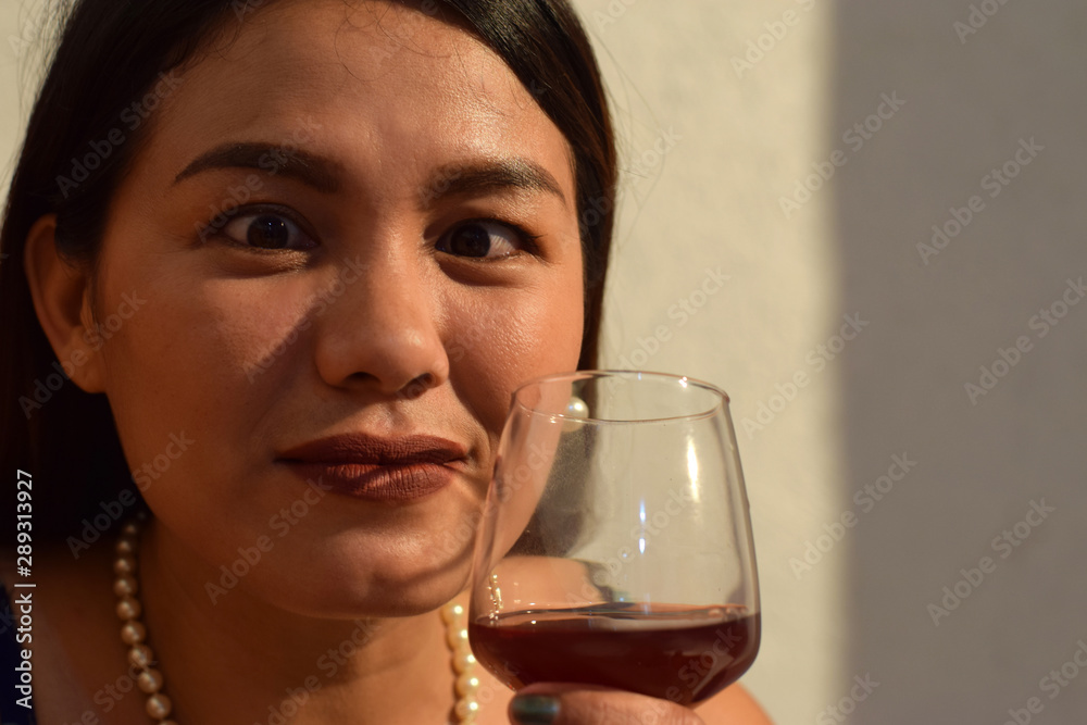 Funny faced, cross eyed beautiful middle aged woman holding wine glass close to her lips