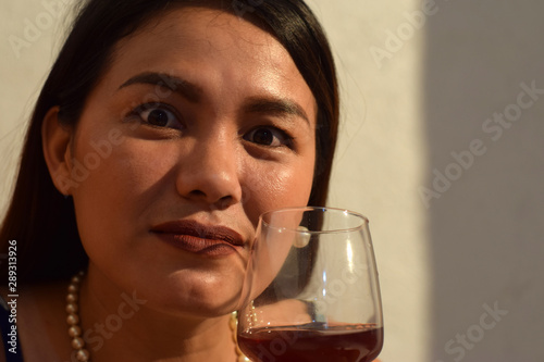 Funny faced, cross eyed beautiful middle aged woman holding wine glass close to her lips photo