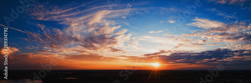 Wide panorama of sunset sky with clouds and sunlight over farm