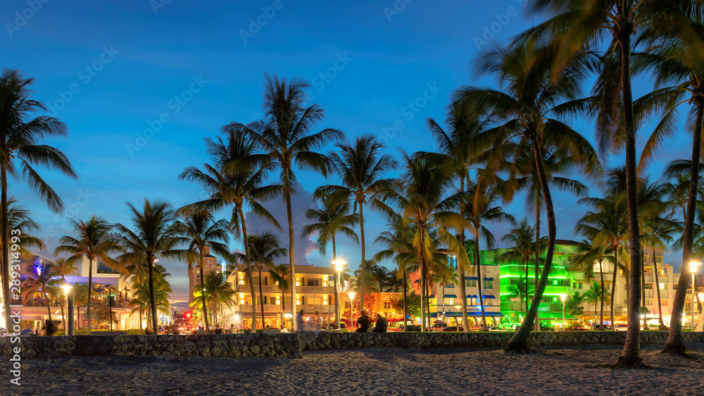 Nightlife in Miami Beach, Florida - palm trees, hotels and restaurants at sunset on Ocean Drive.