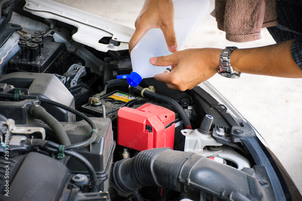 Man or auto mechanic worker hands add distilled water to car battery. Checking and maintenance service the car battery. Man or auto mechanic worker hands add distilled water to car battery. Checking and maintenance service the car battery.