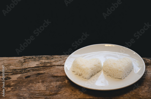 Jasmine rice is arranged in two heart shapes in white dish and on a old wooden table and black background, Selective focus, Vintage style.