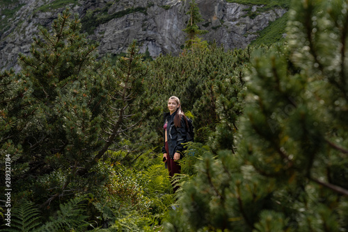 Young girl traveler in balck jacket standing among coniferous forest in the mountains, active lifestyle concept