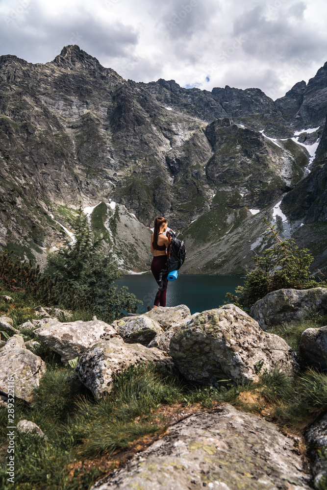 Young girl traveler in red sportswear removes a backpack among the mountains on the background of lake