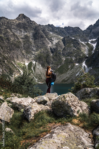 Young girl traveler in red sportswear removes a backpack among the mountains on the background of lake