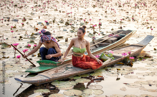 Smiling Young Woman In Traditional Clothing Holding Lotus While Sitting On Boat In Lake against sunset © FotoArtist