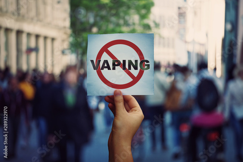 Human hand holding a protest banner stop vaping message over a crowded street background. Banning flavored vaping products to discourage people from smoking electronic cigarettes. Health risk concept. photo