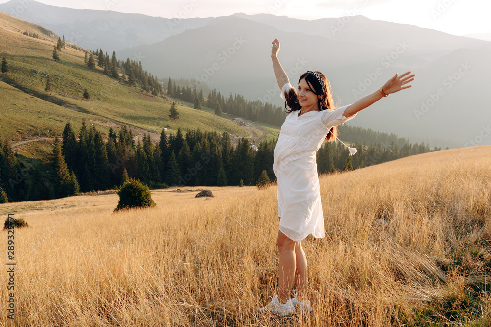 Stylish girl in rustic dress smiling and waving hair in sunny meadow in mountains. Portrait of happy boho woman in countryside at sunset, positive vibes, rural simple life. Atmospheric image Stylish girl in rustic dress smiling and waving hair in sunny meadow in mountains. Portrait of happy boho woman in countryside at sunset, positive vibes, rural simple life. Atmospheric image