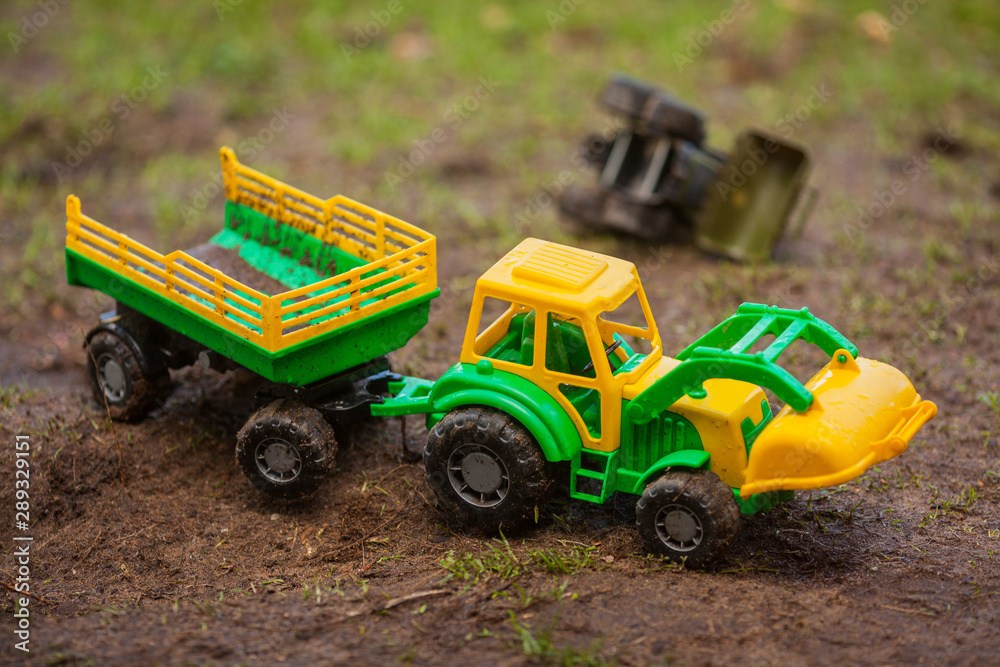 Fototapeta premium The toy tractor is working. Green and yellow tractor with a trailer. Tractor with a bucket, toy.