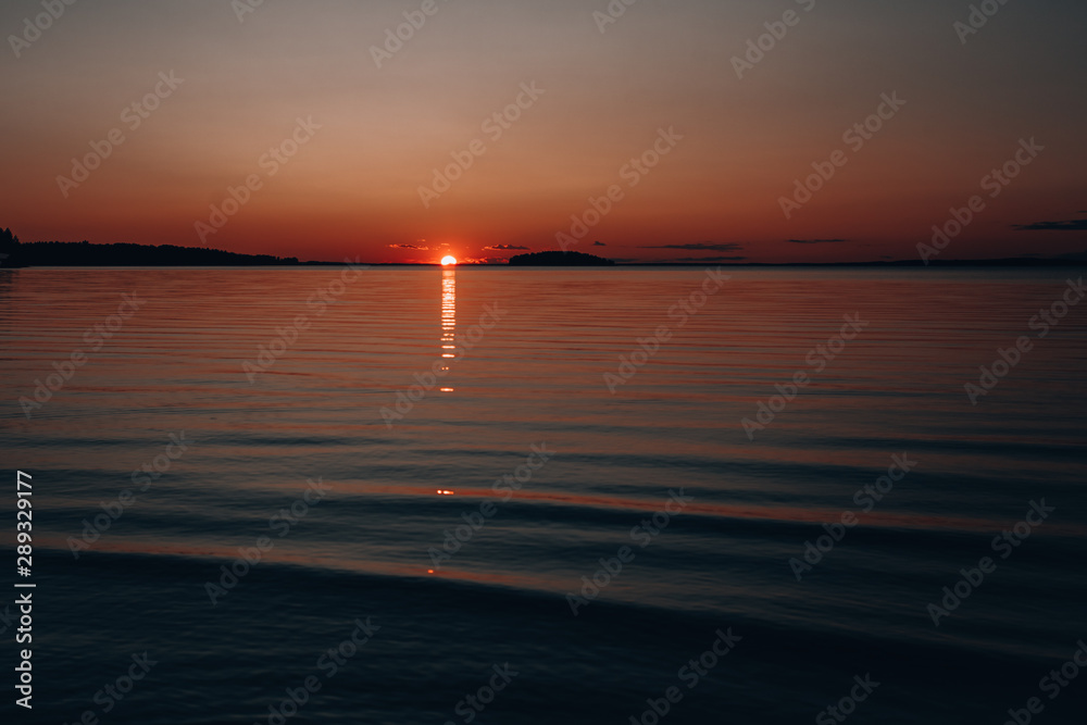 Sunset on the lake. Beautiful sunset by the water. Photo background with the setting sun in the dark.