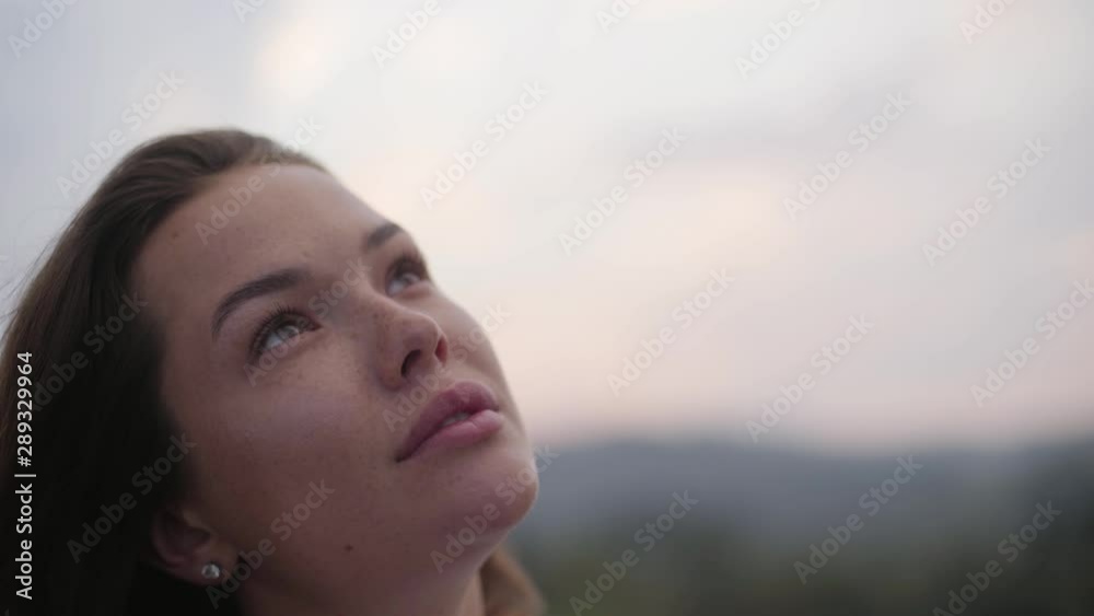 Close-up face of young woman with freckles on her face looking up. The girl spending time outdoors. Connection with nature Close-up face of young woman with freckles on her face looking up. The girl spending time outdoors. Connection with nature