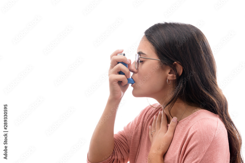 Young caucasian brunette girl with pink shirt suffers from asthma inhaling with an inhaler. isolated in white background. Young caucasian brunette girl with pink shirt suffers from asthma inhaling with an inhaler. isolated in white background.