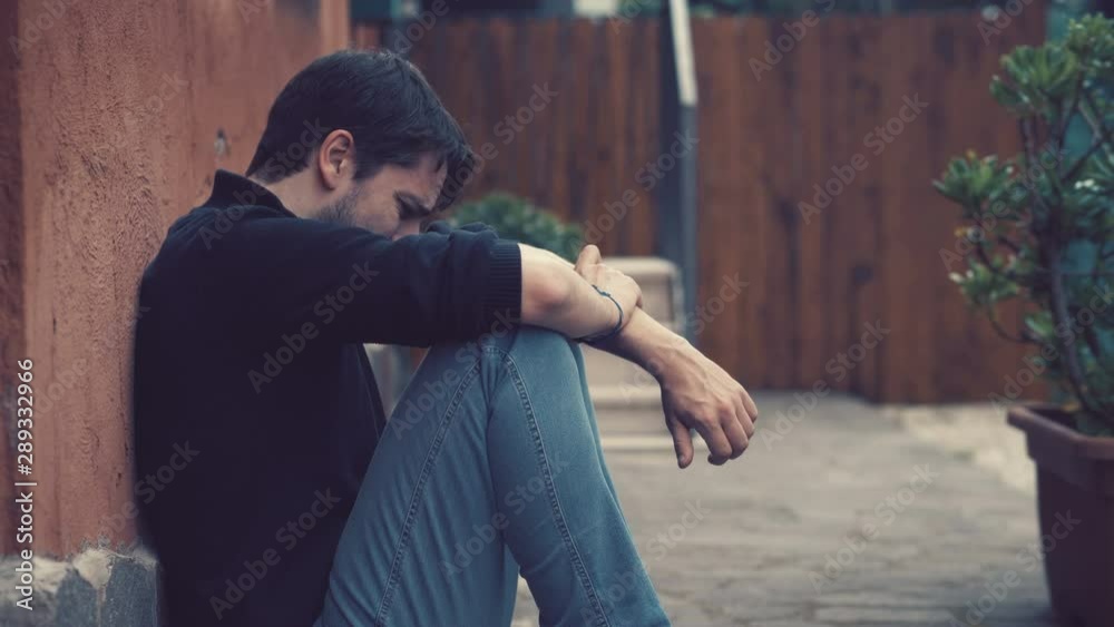Desperate crying young man sitting on the ground. Desperation,solitude-outdoor