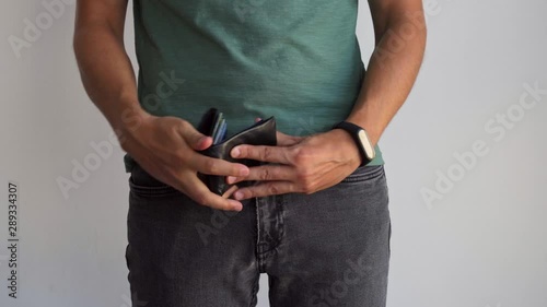 A man in a T-shirt and jeans takes his wallet out of his pocket and shows its contents. A man shows a purse without money. photo