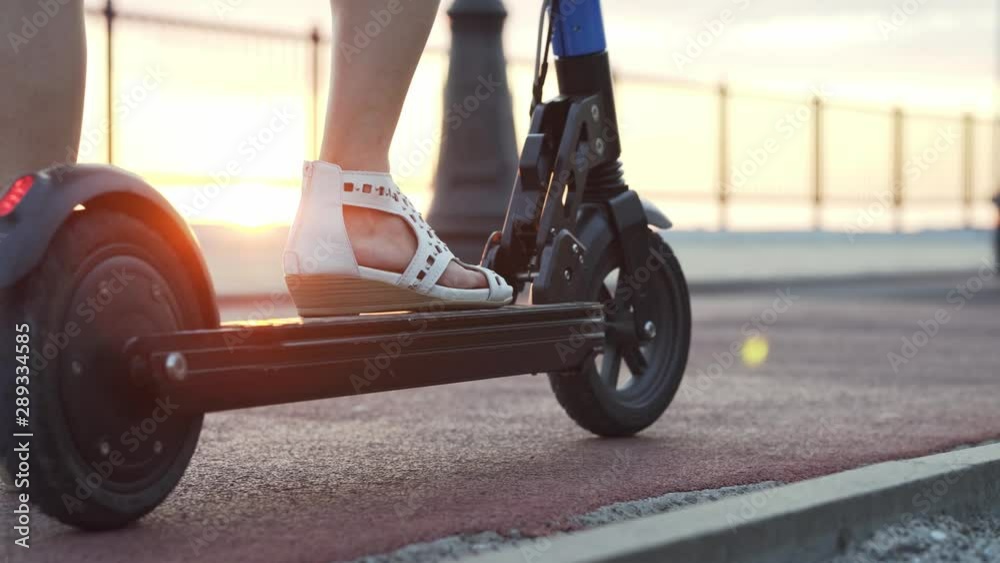 Girl on a scooter starts riding. Girl's legs scooter at sunset closeup. Girl on a scooter starts riding. Girl's legs scooter at sunset closeup.