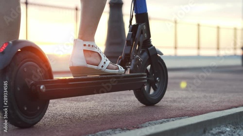 Girl on a scooter starts riding. Girl's legs scooter at sunset closeup.