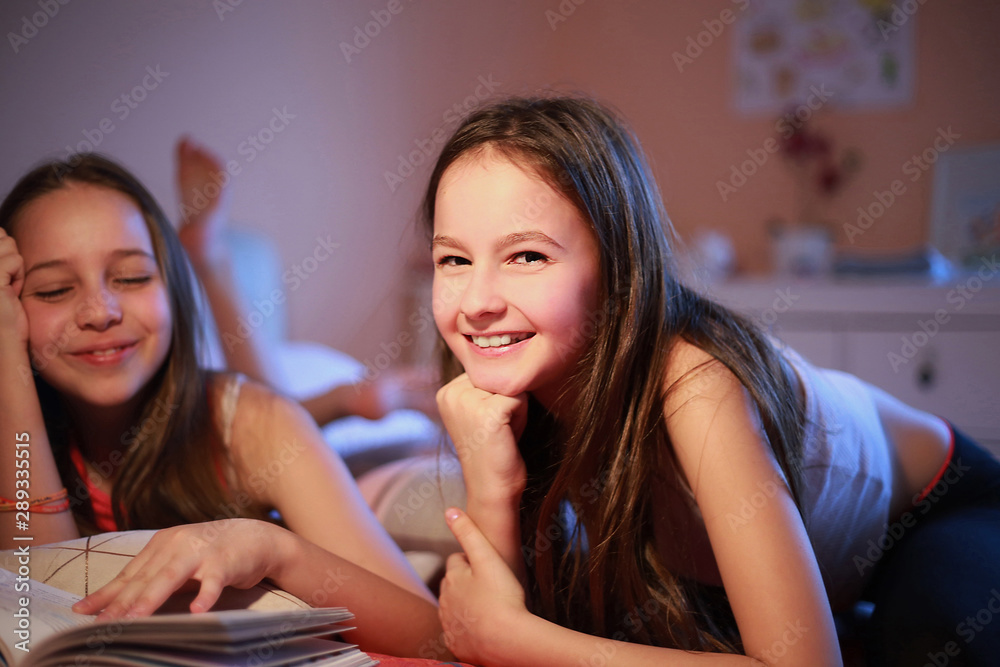 Teenage Girls reading and watching book on bed at home Teenage Girls reading and watching book on bed at home