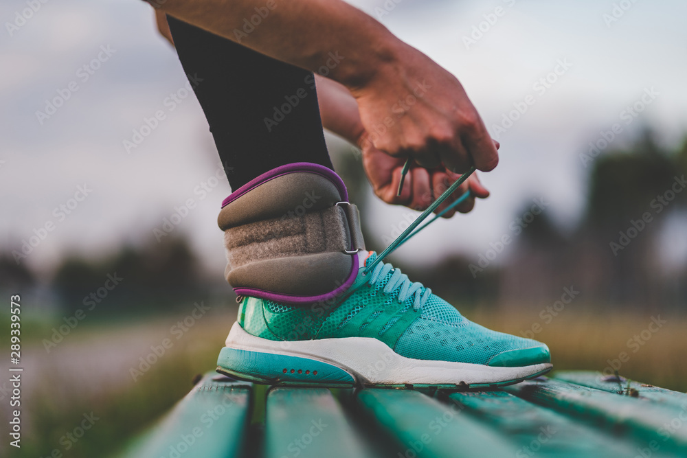 Fototapeta premium Athletic woman tying shoelaces on sneakers while walking with weights during workout outdoor.
