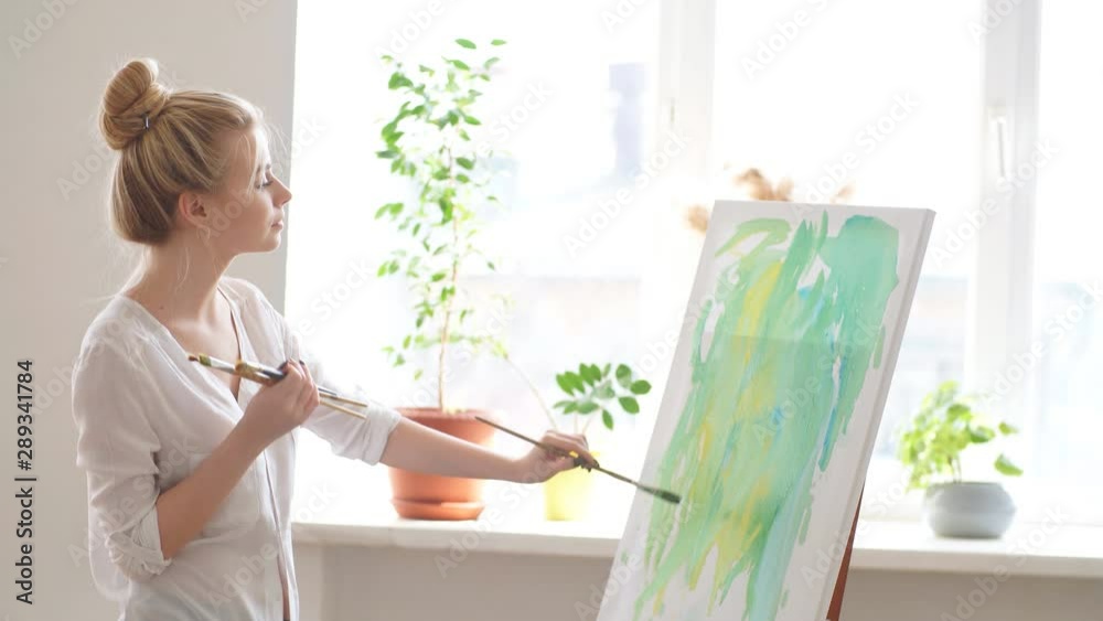 Light room for painting. Woman standing on the corner of the room in front of the easel Light room for painting. Woman standing on the corner of the room in front of the easel
