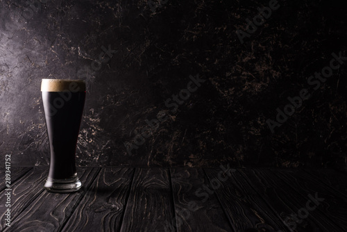 glass of dark beer on wooden table with shadow