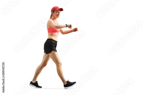 Smiling young female walking and looking at her smart sports bracelet