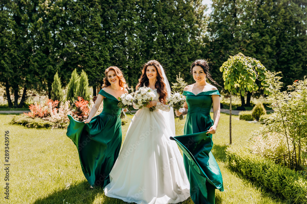 Pretty bride with her girlfriends in beautiful dresses dancing in the park.
