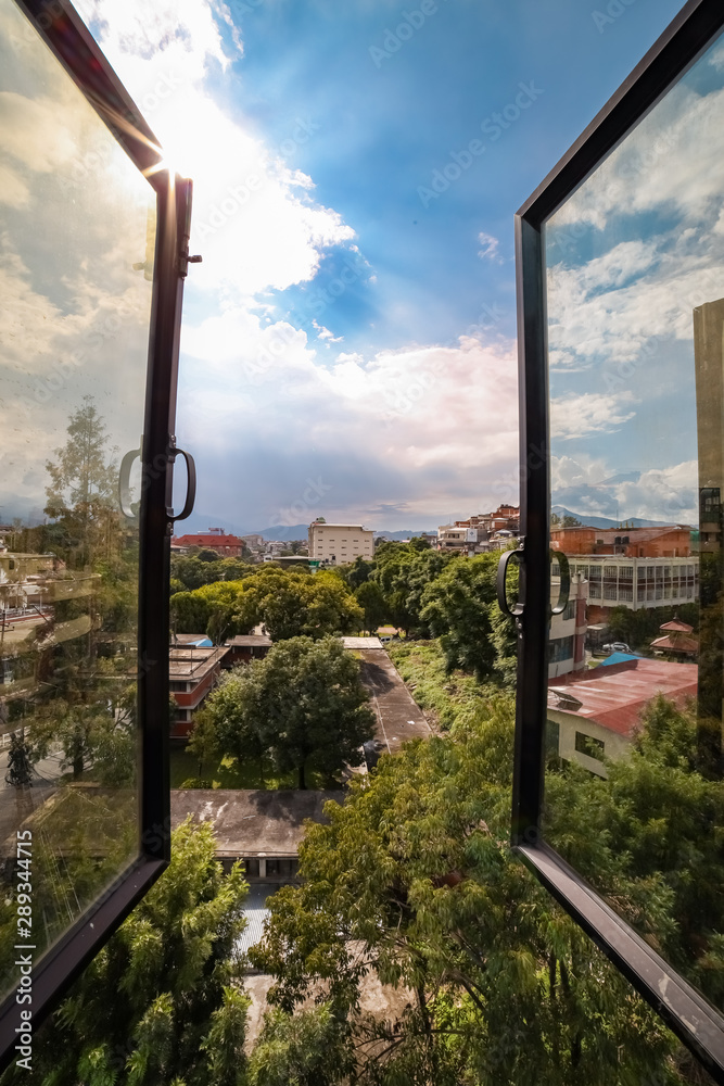 Open window showing green trees, blue sky and houses on a clear day Open window showing green trees, blue sky and houses on a clear day