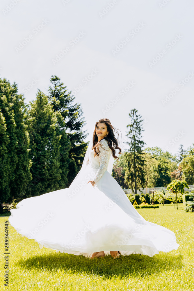 Cute bride in white dress whirls in the park
