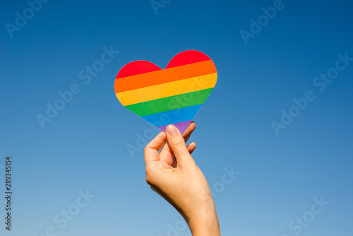 Woman holds in hands a heart in the colors of the rainbow. Young beautiful girl. LGBT history month. Pride Month. Lesbian Gay Bisexual Transgender. LGBT flag. Love, human rights, tolerance. LGBTQ+