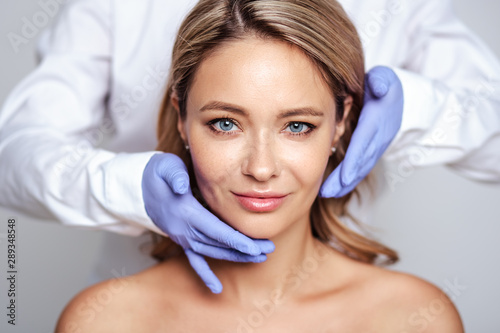Close up portrait of young blonde woman with cosmetologyst hands in a gloves. Preparation for operation or procedure. Perfect skin, spa and care
