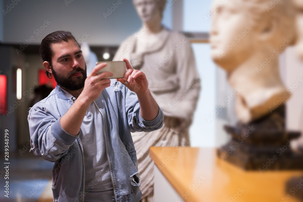 Adult male visitor using phone in sculptures exposition at museum