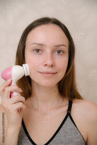 Young woman uses an electric brush to deeply clean her face