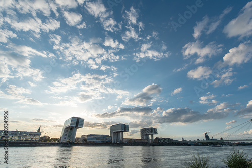 panoramic skyline view of the rhine shore in cologne with river in the foreground and crane houses with cathedral in the back on a sunny afternoon in september