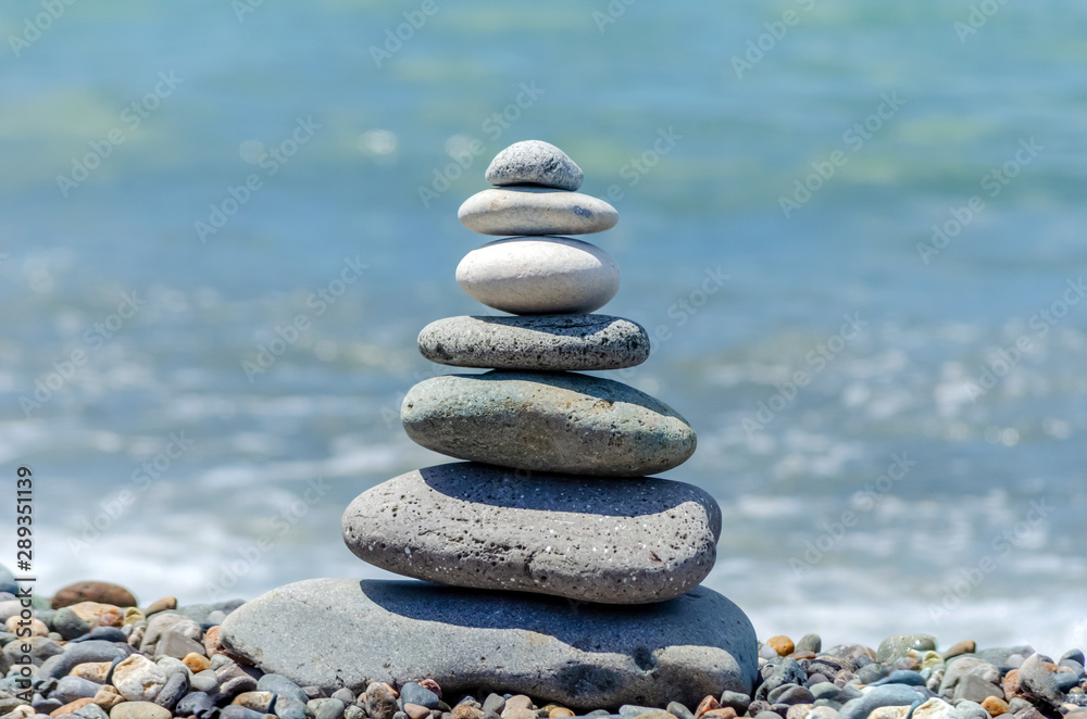 pyramid of sea pebbles on the beach against the backdrop of the sea wave in sunny day. concept of balance harmony and meditation. copy space pyramid of sea pebbles on the beach against the backdrop of the sea wave in sunny day. concept of balance harmony and meditation. copy space