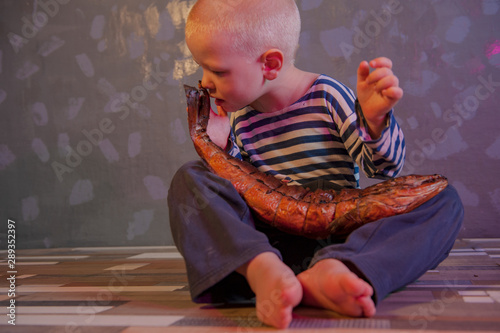 Little blond boy shows big smoked fish. Child wants to catch big fish in ariver. Concept of organic food. photo