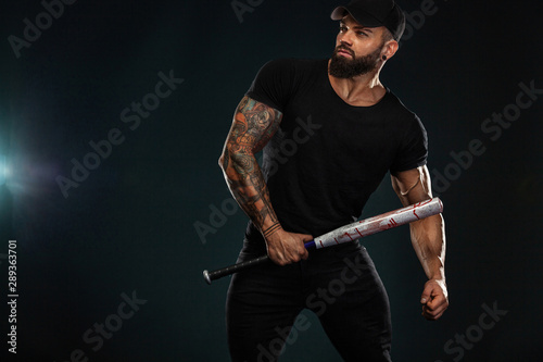 Strong and fit man bodybuilder with baseball bat in black t-shirt. Sporty muscular guy athlete. Sport and fitness concept. Men's fashion.