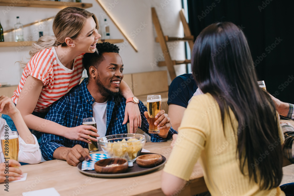 young woman hugging african american man near multicultural friends in pub