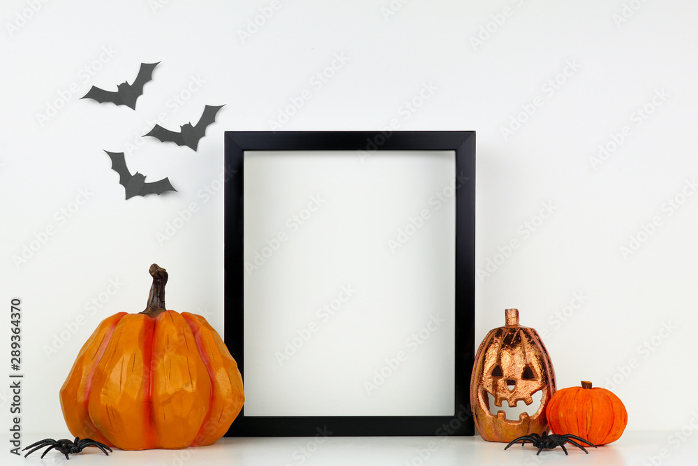 Mock up black frame with Jack o Lantern and pumpkin decor on a shelf or desk. Halloween concept. Portrait frame against a white wall with bats. - obrazy, fototapety, plakaty 