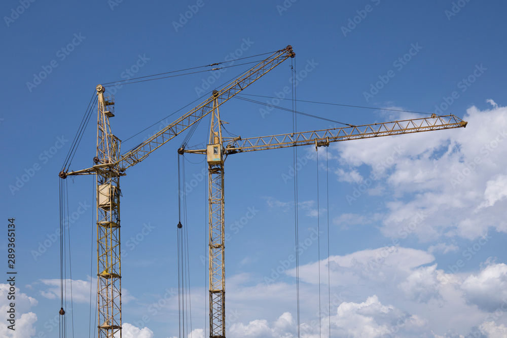 Copy space between two construction cranes against blue cloudy sky Copy space between two construction cranes against blue cloudy sky