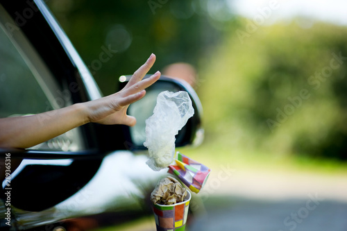 A young woman throws waste from the car - a coffee cup and a bag. Environmental pollution, selective focus, backlight. Copy space
