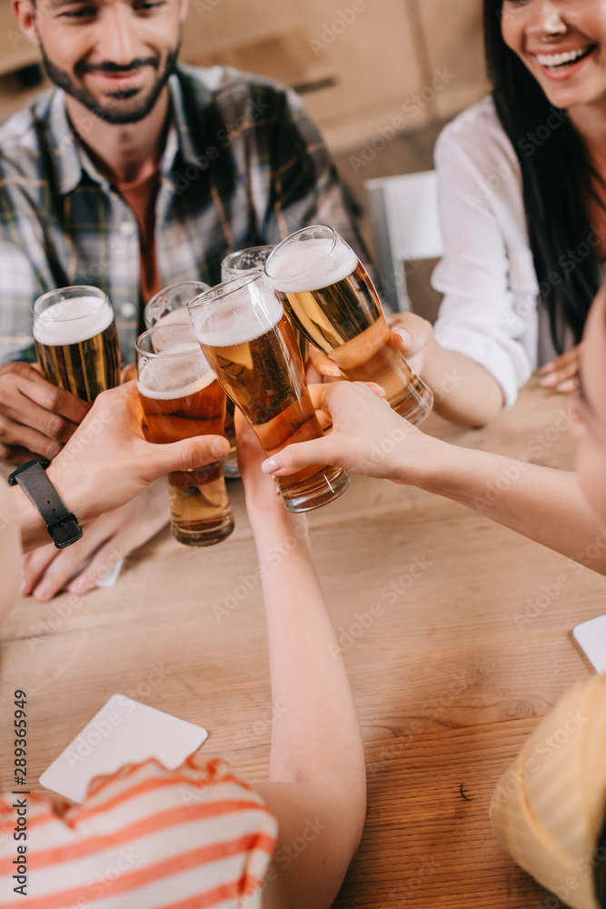 partial view of multicultural friends clinking glasses of light beer in pub