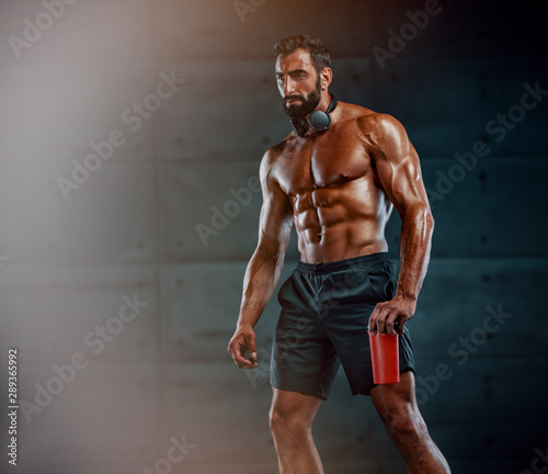 Handsome Muscular Men Holding Protein Drink , Wireless Headphones are around his neck