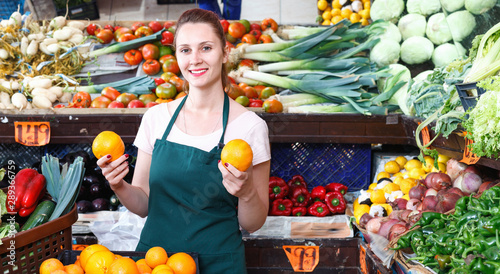 Seller female is holding oranges on her workplace in the market.