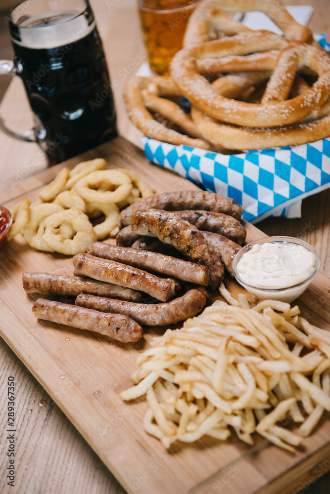 fried sausages, onion rings, french fries, pretzels and mugs with beer on wooden table in pub fried sausages, onion rings, french fries, pretzels and mugs with beer on wooden table in pub
