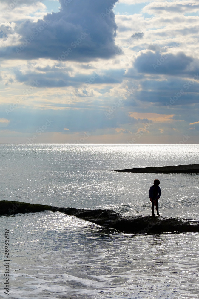 A six year old unrecognisable boy alone walking along a jetty in the sea.
