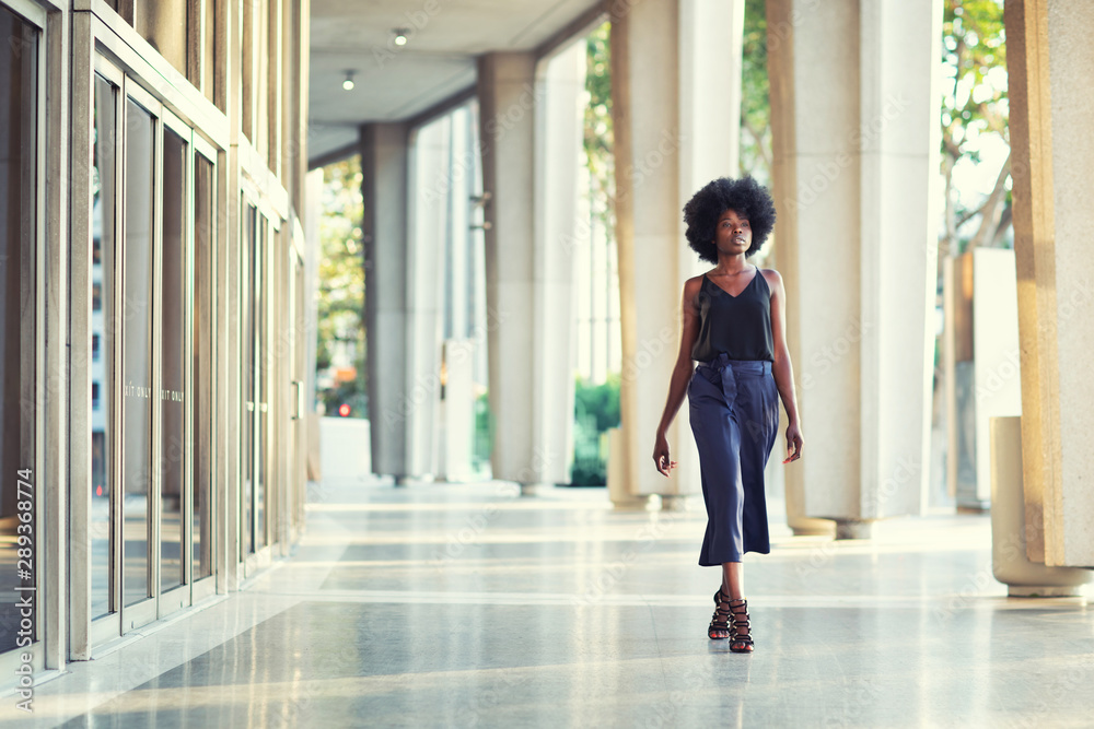 A young fashionable Afro-American woman confidently walking down the hall outside the financial building